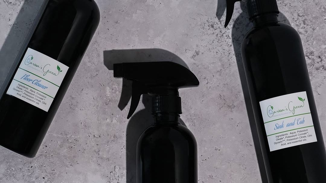 Black spray bottles of handmade cleaner lying on a grey stone surface, with hand-labeled stickers.